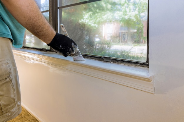 Mão de trabalhador com luvas na moldura da janela de pintura