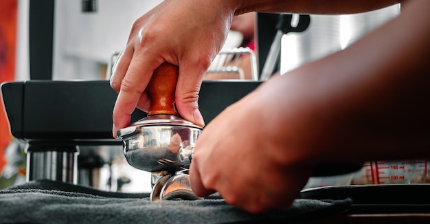 Mão de um barista segurando um filtro e uma adulteração de café fazendo um café expresso usando uma adulteração