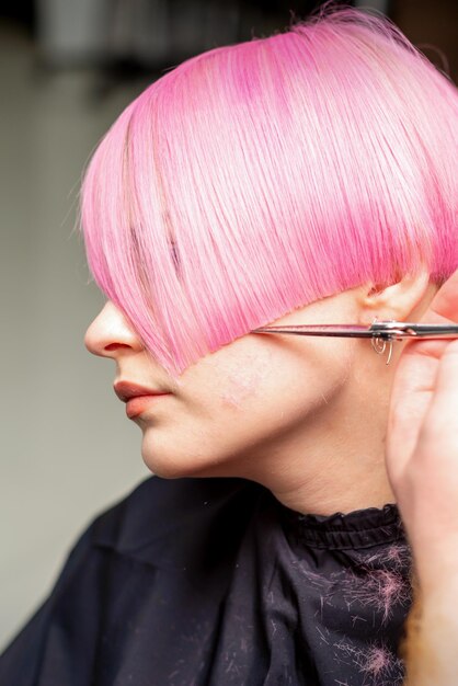 Mão de um cabeleireiro cortando rosa curto com cabelo de tesoura em um salão de cabeleireiro, close-up, vista lateral.