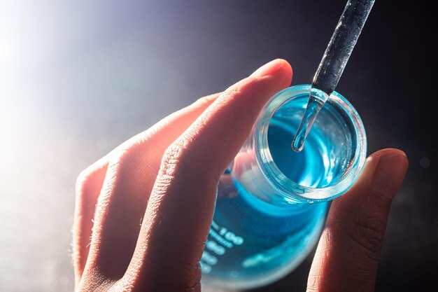 Mão de um cientista segurando um frasco com vidraria e tubos de ensaio no fundo do laboratório químico