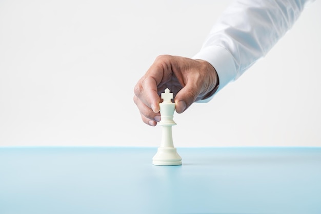 Mão de um empresário colocando figura de xadrez branco do rei na mesa azul