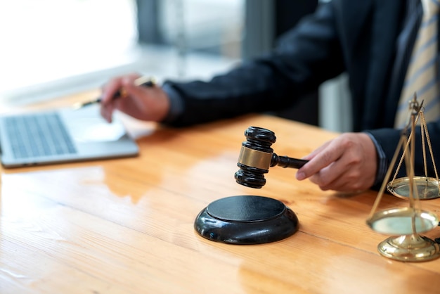 Mão de um empresário ou advogado segurando um martelo de juiz trabalha usando um teclado de laptop, a balança é colocada na mesa do escritório.