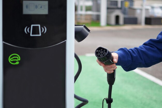 Mão de um homem carregando um carro elétrico em uma estação de carregamento