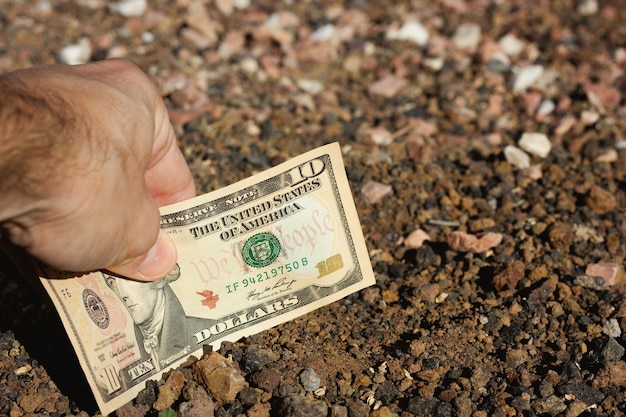 Mão de um homem colocando uma nota de dez dólares no solo, terreno, conceitos de projeto de barganha de investimento de terras