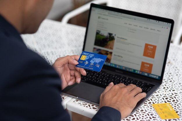 Foto mão de um homem de negócios que prende uma informação do cartão e da impressão de crédito em um computador.