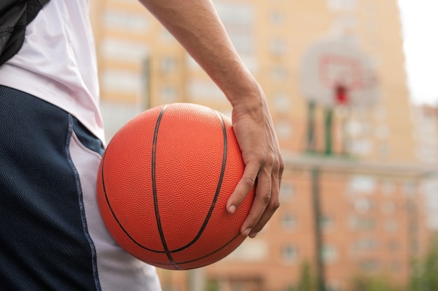 Mão de um jovem jogador de basquete profissional segurando uma bola enquanto vai treinar no playground