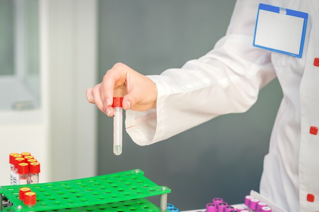 Mão de um técnico de laboratório ou enfermeira tira um tubo de ensaio de sangue vazio da prateleira do laboratório de pesquisa