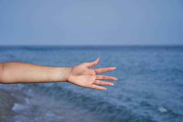 mão de uma jovem com unhas compridas com o mar ao fundo