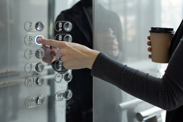 Mão de uma jovem empresária apertando o botão do elevador enquanto voltava ao escritório no quinto andar no intervalo para o café