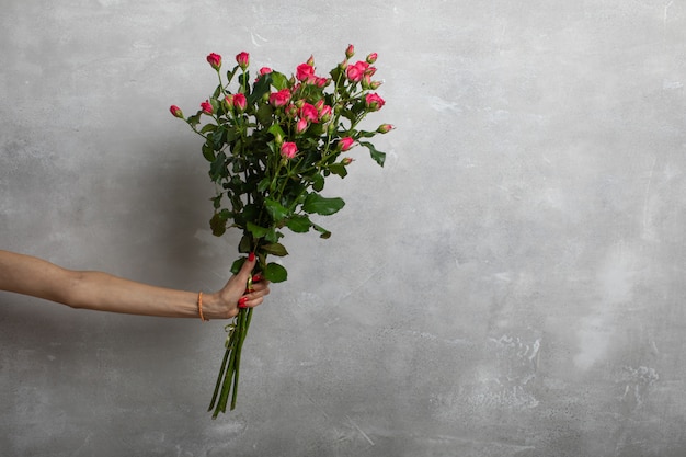 Mão de uma jovem garota segurando um buquê de rosas