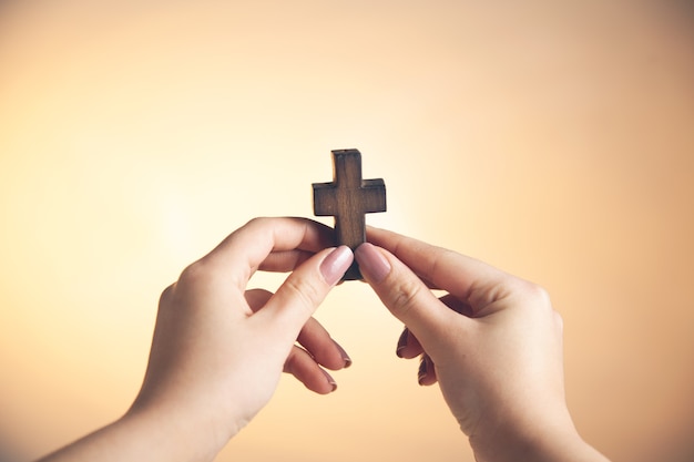 Mão de uma jovem segurando uma cruz de madeira