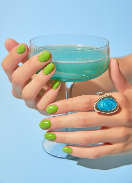 Mão de uma linda mulher com design de unhas verdes de verão segurando salão de beleza de manicure e pedicure de vidro