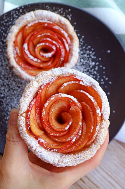 Mão de uma mulher colhendo uma linda mini tartelete de maçã com açúcar de confeiteiro