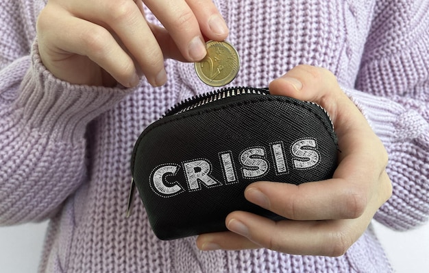 Mão de uma mulher colocando moedas na carteira preta com a palavra Crise