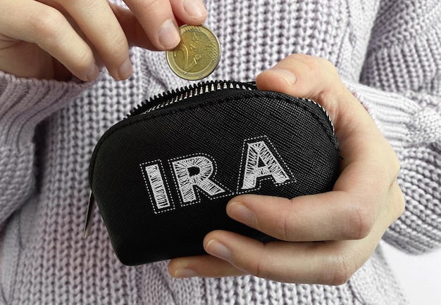 Mão de uma mulher colocando moedas na carteira preta com a palavra IRA
