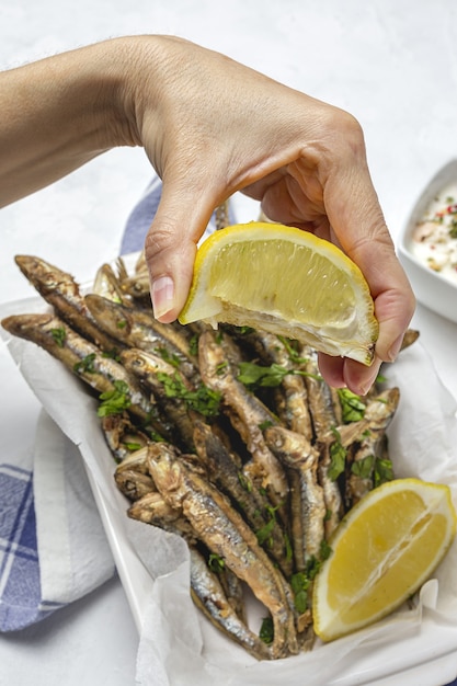 Mão de uma mulher com anchovas fritas com limão e salsa. conceito de frutos do mar