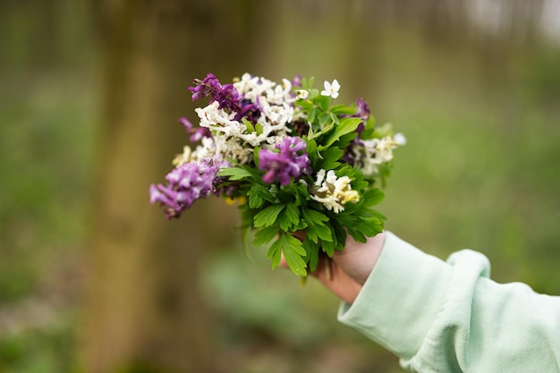 Mão de uma mulher com buquê de primavera de flores na floresta Conceito de lazer ao ar livre