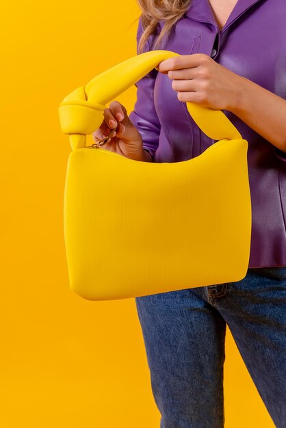 Mão de uma mulher com uma bolsa amarela em um estúdio de moda de fundo amarelo