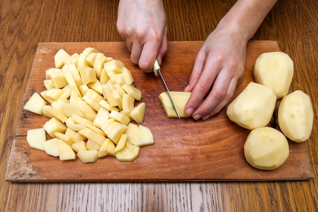 Mão de uma mulher com uma faca cortando batatas