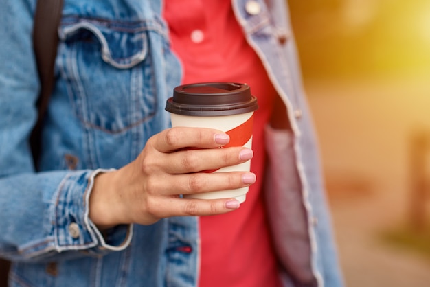 Mão de uma mulher com uma xícara de café de papel levar em uma rua da cidade
