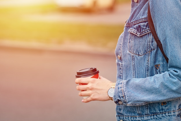 Mão de uma mulher com uma xícara de café de papel levar em uma rua da cidade