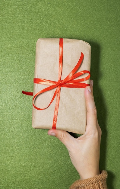 Mão de uma mulher entregando presente com papel reciclado sobre fundo verde