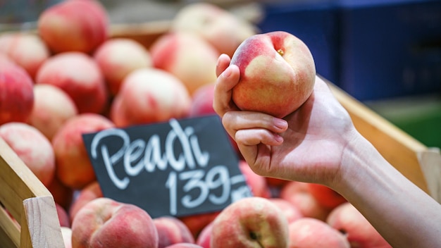 Mão de uma mulher escolhendo frutas de pêssego no supermercado