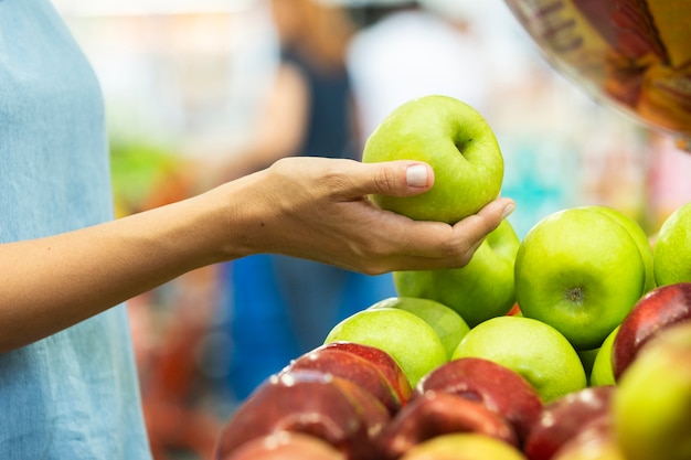 Mão de uma mulher escolhendo maçã verde no supermercado.