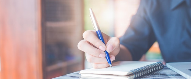 Mão de uma mulher escrevendo em um bloco de notas com uma caneta no escritório