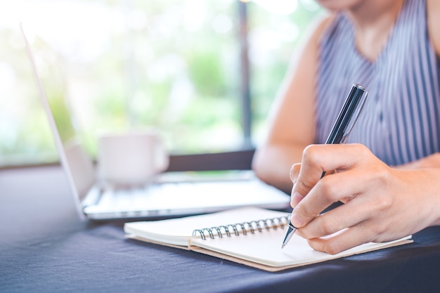 Mão de uma mulher escrevendo no bloco de notas com uma caneta no escritório