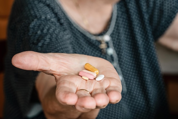 Mão de uma mulher idosa segurando cinco pílulas ou remédios diferentes