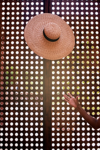 Foto mão de uma mulher jogando um chapéu em um fundo geométrico