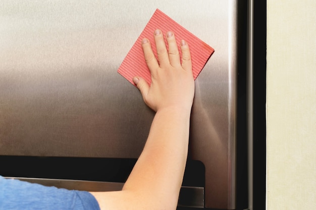 Mão de uma mulher limpando geladeira cinza prata com pano rosa