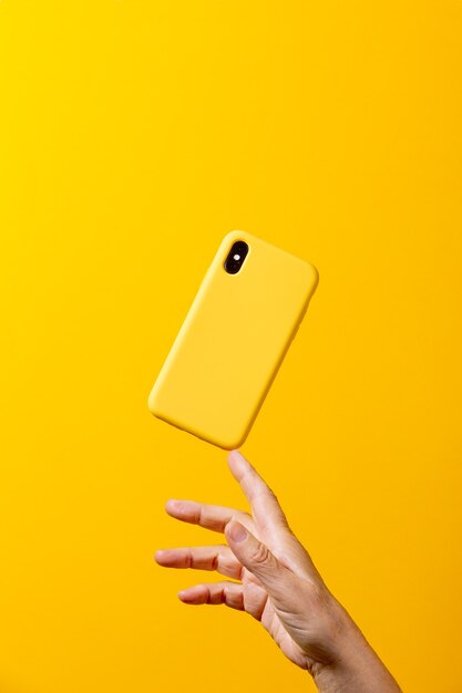 Foto mão de uma mulher madura segurando um smartphone amarelo com uma caixa amarela e um dedo sobre um fundo amarelo