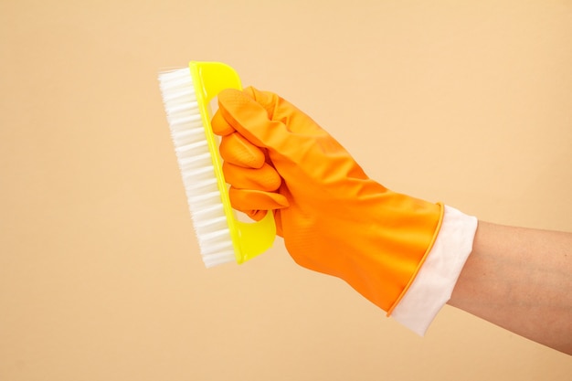 Mão de uma mulher na luva protetora de borracha com escova de plástico em fundo bege. conceito de lavagem e limpeza.