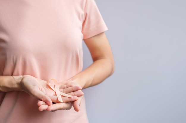 Mão de uma mulher segurando a fita de pêssego para o mês de conscientização do câncer uterino de setembro Conceito de saúde e dia mundial do câncer