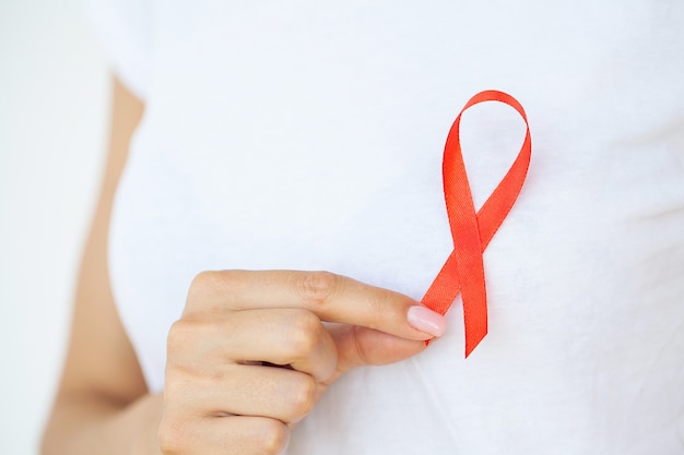 Mão de uma mulher segurando a fita vermelha HIV, fita de conscientização do dia mundial da Aids.