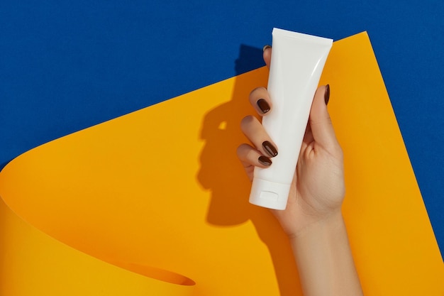 Mão de uma mulher segurando cosmético em fundo laranja com espaço para cópia Conceito de tratamento de beleza