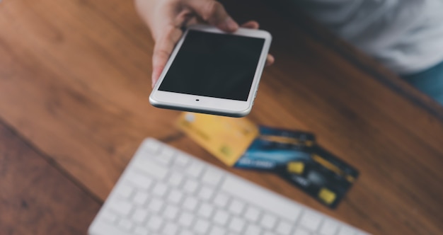 Mão de uma mulher segurando o cartão de crédito e o celular com o computador para internet banking e o conceito de compra online.