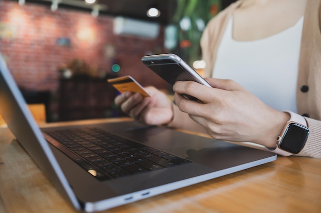 Mão de uma mulher segurando o cartão de crédito e usando o smartphone laptop no café para pagar on-line usando o serviço de internet banking Conceito de compras on-line