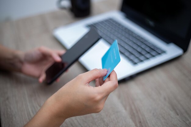 Mão de uma mulher segurando o celular e o cartão de crédito na frente do laptop