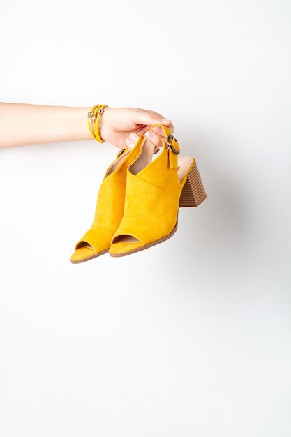 Mão de uma mulher segurando os sapatos femininos amarelos.