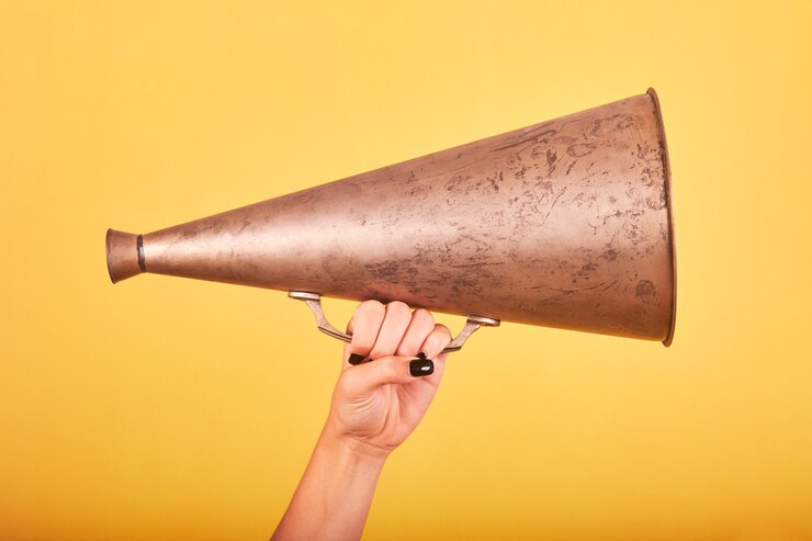 Foto mão de uma mulher segurando um megafone velho em um espaço amarelo