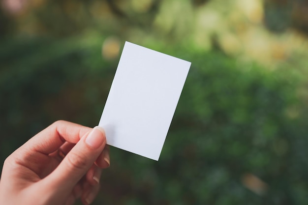 Mão de uma mulher segurando um pequeno papel branco em branco com fundo de natureza turva