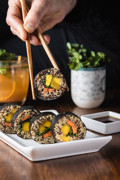 Mão de uma mulher segurando um rolo de sushi vegetariano com pauzinhos de madeira