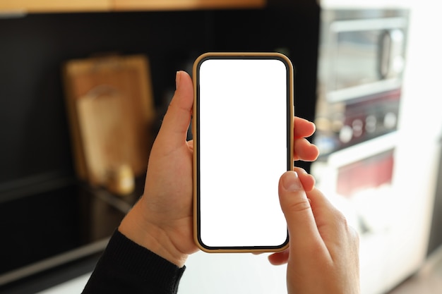 Mão de uma mulher segurando um smartphone com tela branca vertical na cozinha em casa