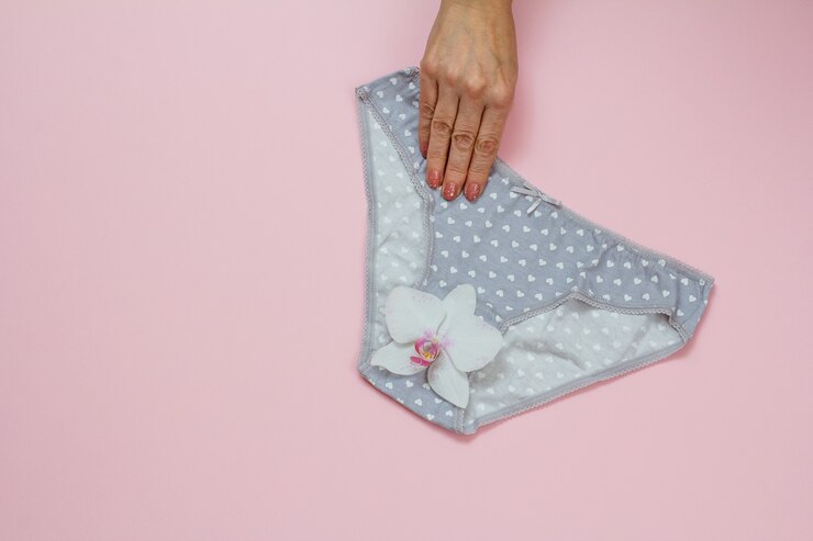 Foto mão de uma mulher segurando uma bela calcinha de algodão cinza em fundo rosa com botão de orquídea. conjunto de roupa interior de mulher. vista superior com espaço de cópia.