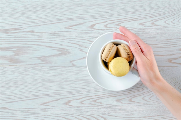 Mão de uma mulher segurando xícara cheia de chocolate doce macaronscookies de limão no prato fundo branco pastelaria confeitaria sobremesas saborosas comida de açúcarespaço de cópia