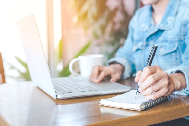 Mão de uma mulher trabalhando em um computador notebook e escrevendo em um bloco de notas