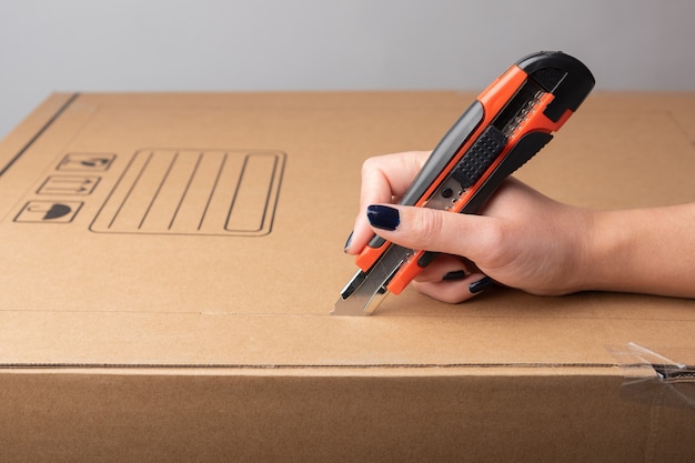 Mão de uma mulher usando uma faca artesanal em uma caixa de papelão com espaço de cópia para informações do tutorial, como texto ou desenho